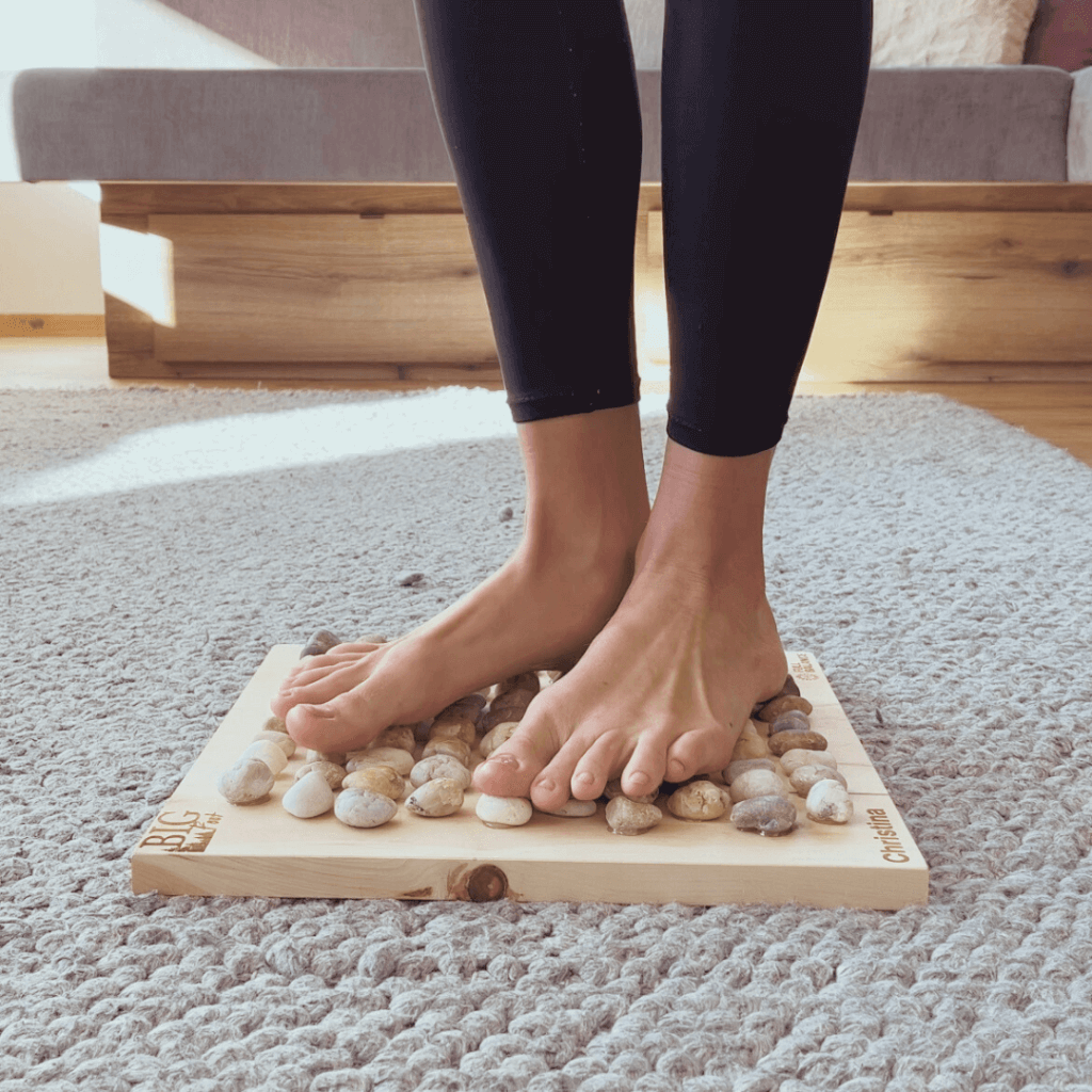 Eine Frau steht Barfuß auf Natursteinen und Zirbenholzbrett - dem Big Foot Vital Board